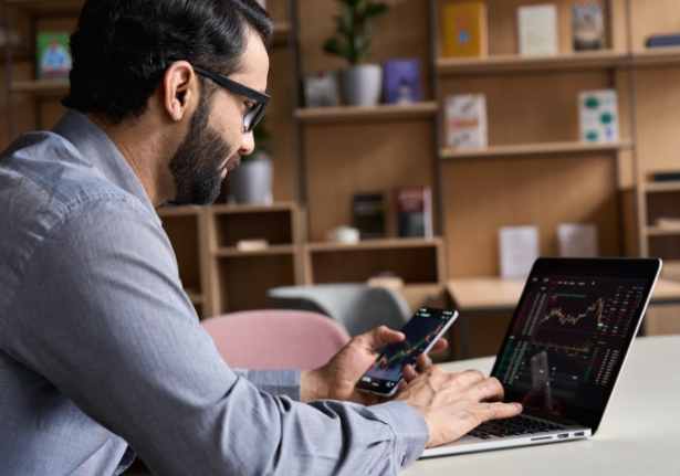 a man trading on mobile and laptop device